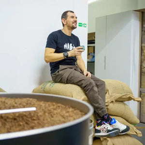 Bogdan Georgescu, vicecampion mondial la prăjirea cafelei, așezat pe saci de cafea, pentru cursul Prăjirea cafelei